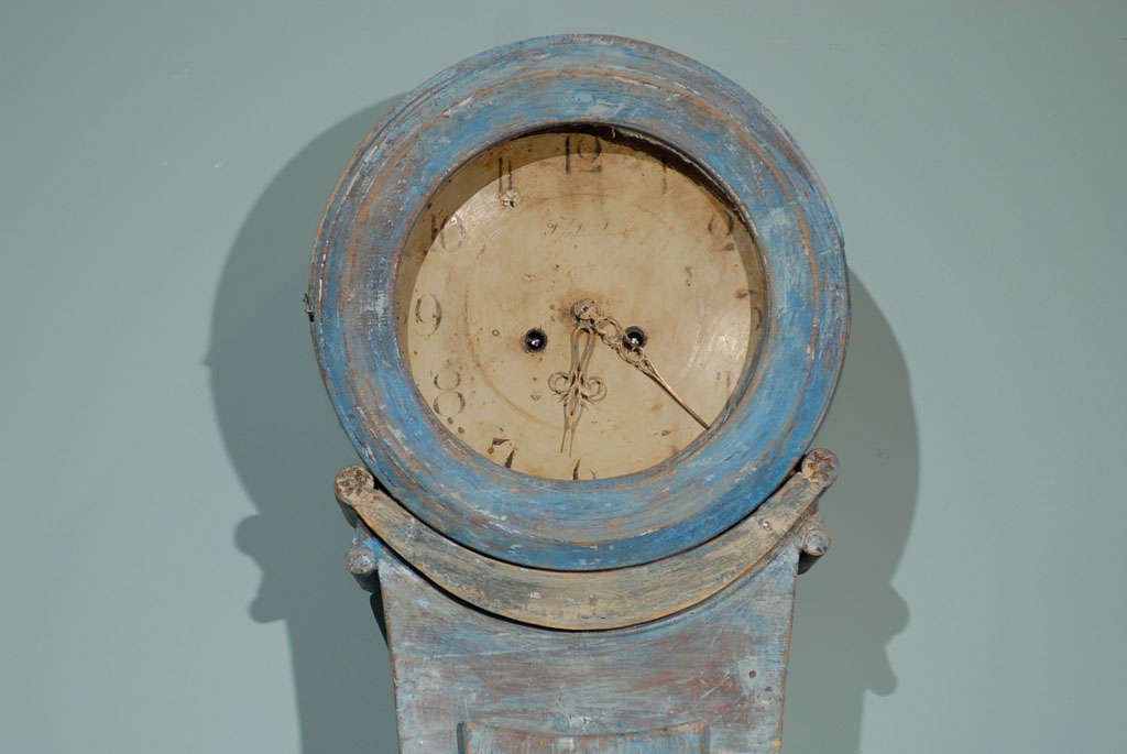 A 19th century Swedish painted wood clock, also commonly called Mora Clock. This clock has very simple and elegant lines, while the paint color is more in the blue tone. Volutes and rosettes decorate the neck and the waste. The clock rests on a flat