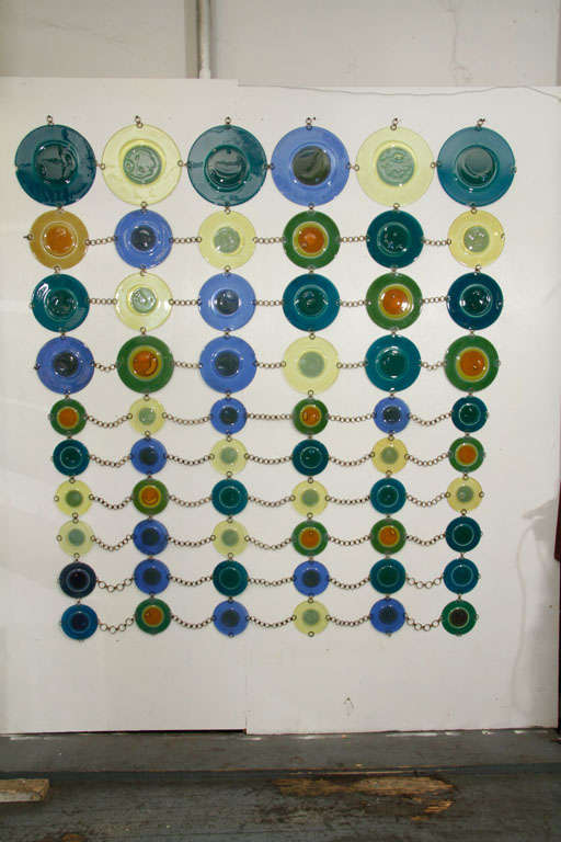 Monumental screen by glass artists Michael and Frances Higgins. The fused glass rondelays are graduated in size and connected by chains of brass rings. The rondelays are three sizes: 11.5