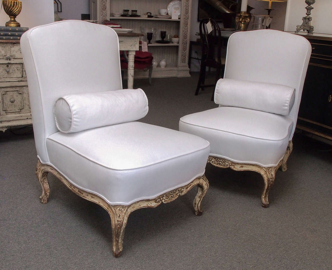 Pair of upholstered slipper chairs, France circa 1930. The padded back and padded seat are raised above a carved wood apron with floral motif having cabriole legs ending in scroll toes.  There is a matching upholstered bolster.