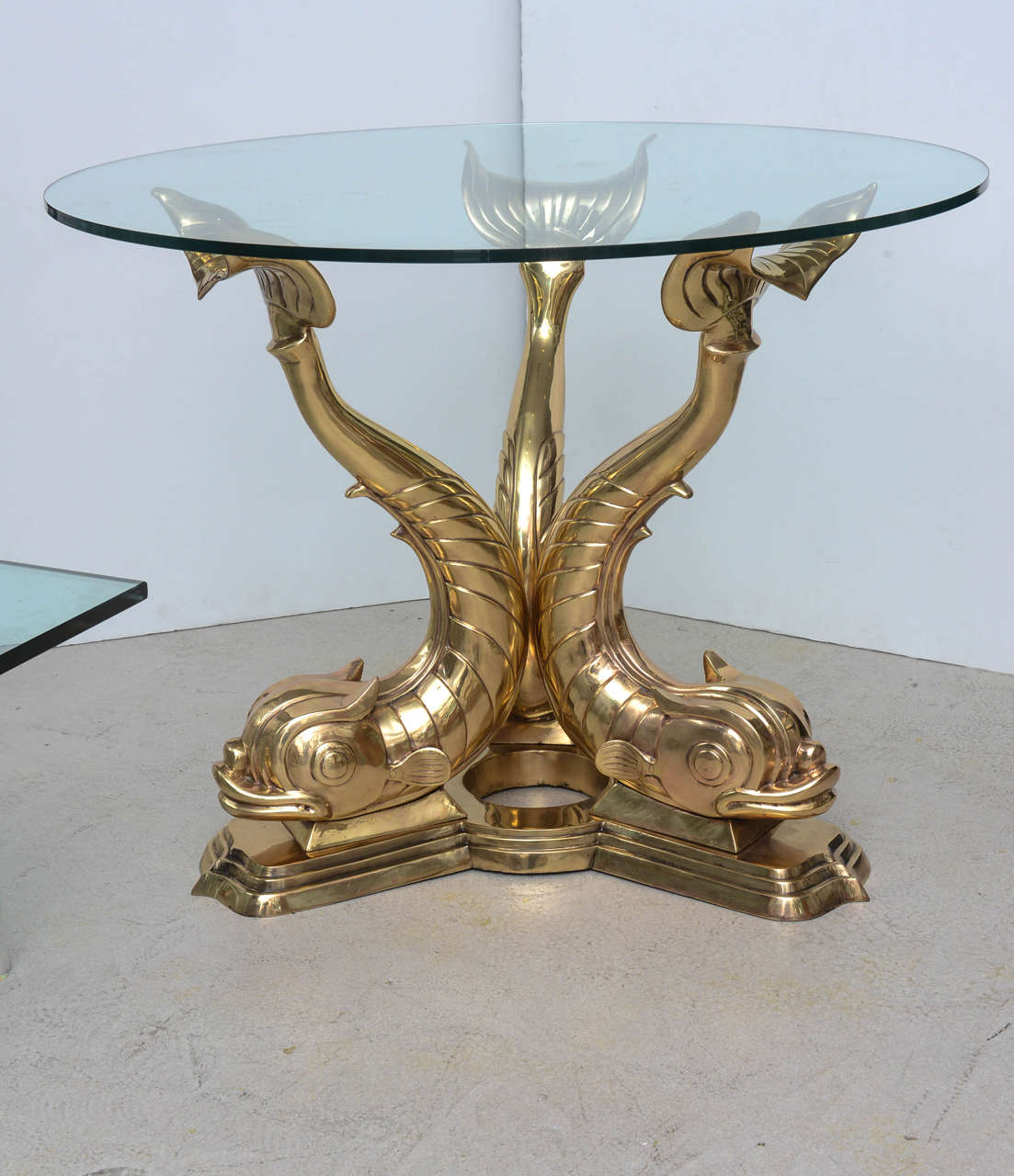 Sculptural stylized brass center table with dolphin motif and circular glass top.