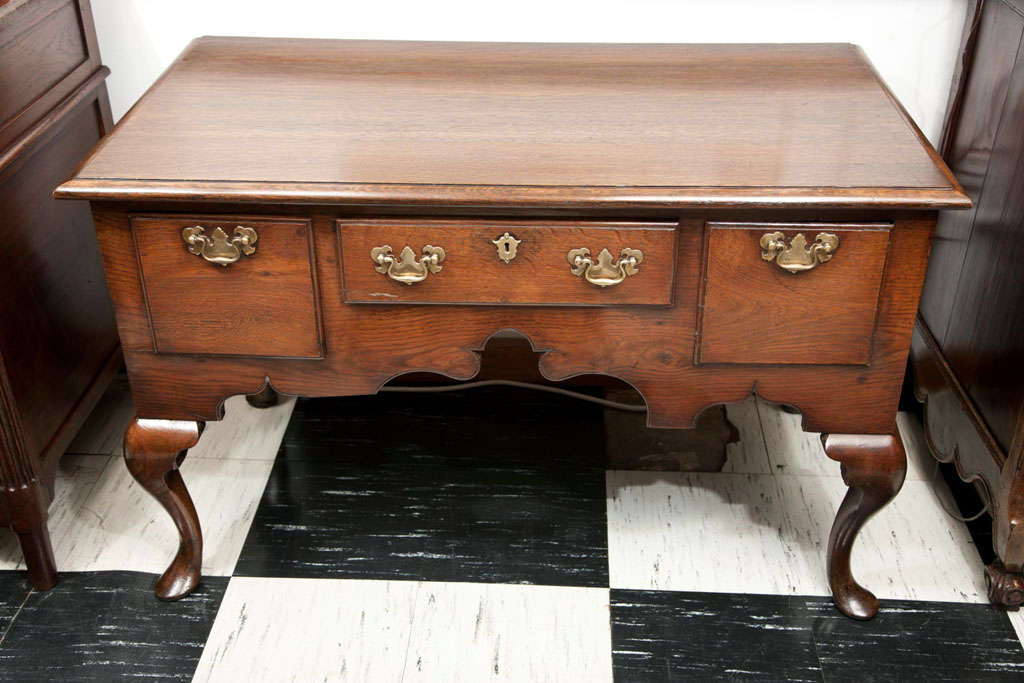 This English, oak lowboy has a large footprint, but small feet. Its generous width of 44 inches is on the large size for a lowboy, but a deep scallop in the apron combined with deeply curved cabriole legs takes some of the visual weight off. Deep