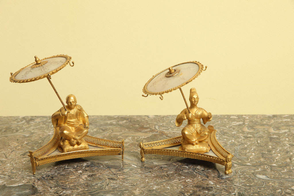 Rare pair of Palais Royale ormolu and mother-of-pearl ring holders, one figure a seated chinoiserie woman the other a seated chinoiserie man on re-entrant triangular bases,, both holding aloft ormolu banded and engraved mother of pearl parasols with