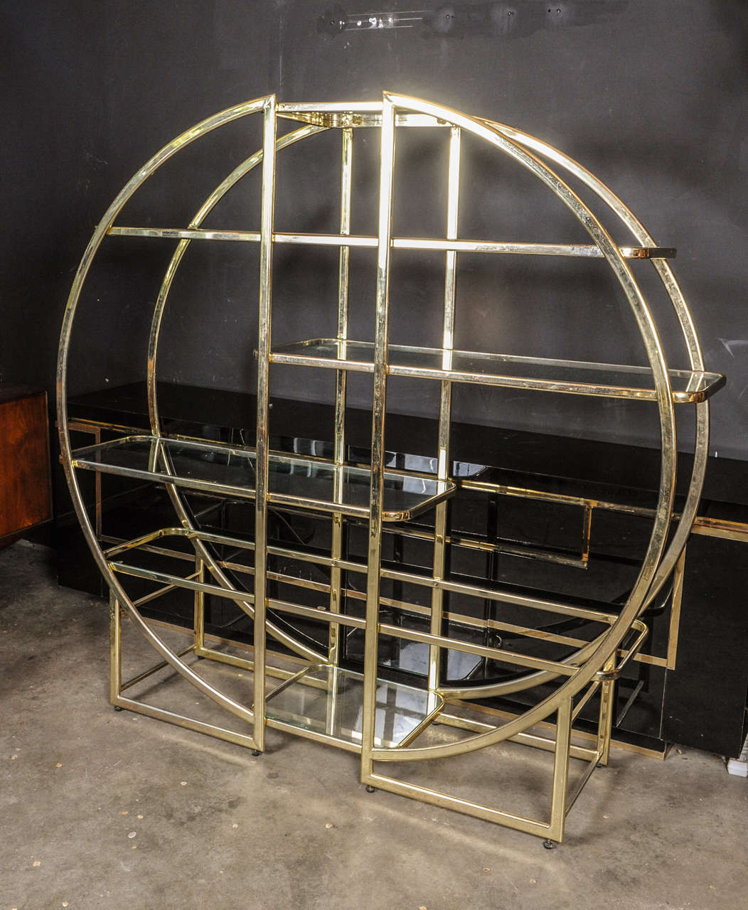 Beautifully shaped round edged book case / etagere / vitrine made of brass and with glass shelves. To be used against a wall or as a stand alone room divider.