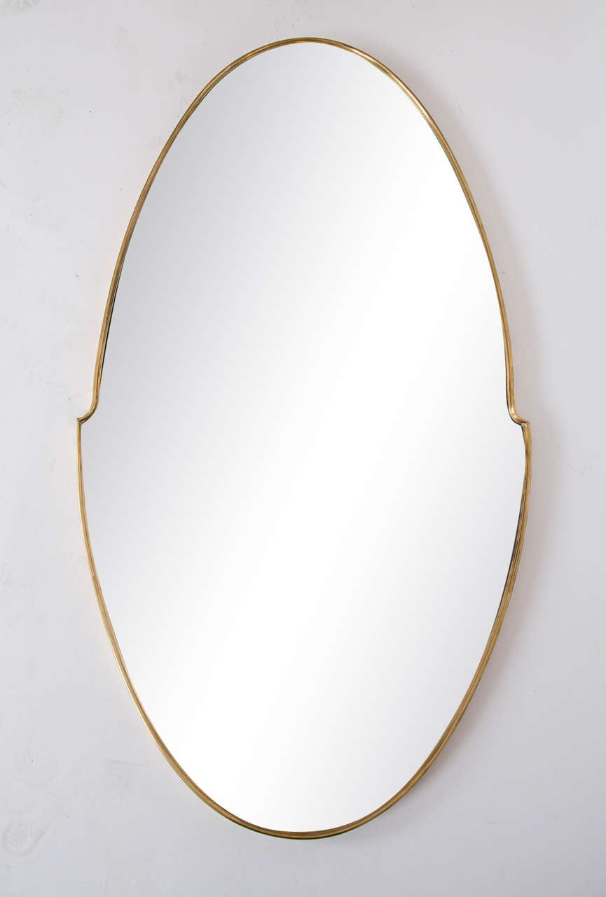 Modern classical shaped oval mirror sits in brass edging.