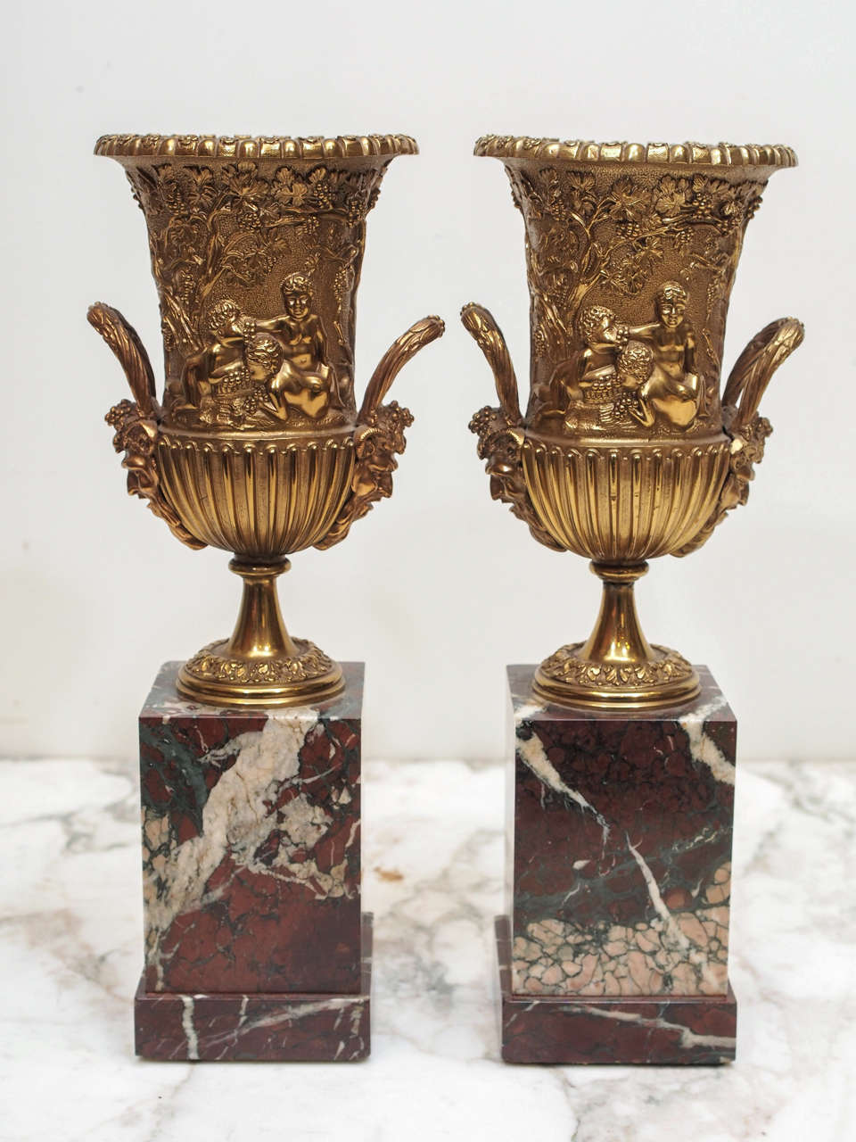 Pair of Cast Classical Handled Urns on rouge marble plinths in the manner of the Grand Tour