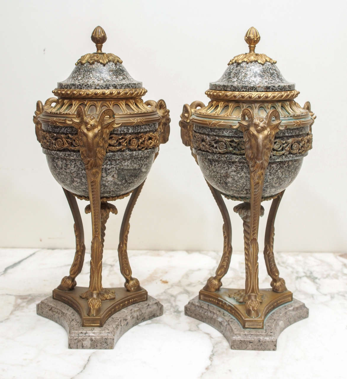 Pair of French Marble and gilt Bronze Cassolet Garniture. In classical form with foliate decoration banding and finial with rams head on trifed monopodial goat hoofs all on a marble plinth.