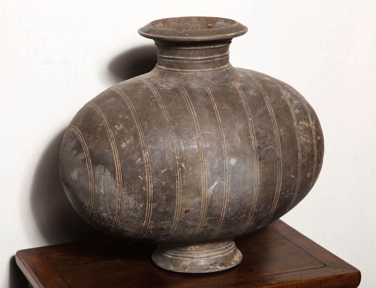 This rare terracotta cocoon jar with uncommon incised bands was made in China during the Western Han dynasty (206 B.C. - 9 A.D.). The jar features a dark grey color with lighter vertical incised bands on its belly. The cocoon shape refers to the