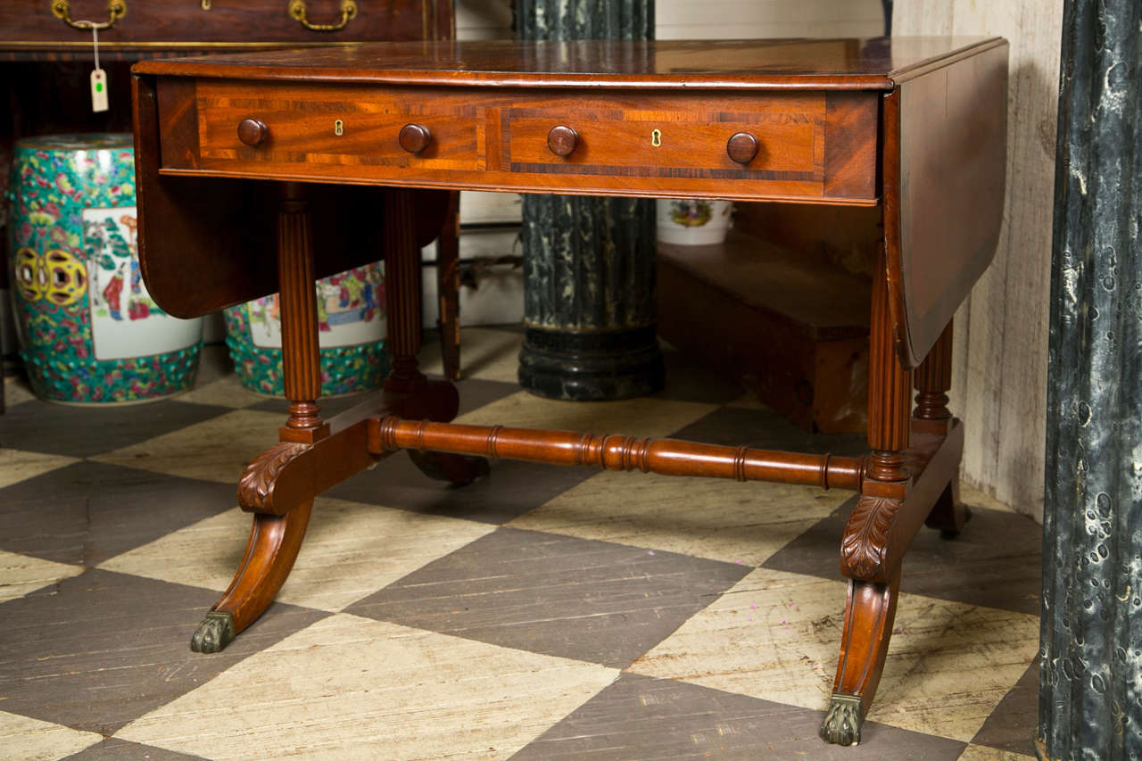 a mahogany sofa table with cross banded top and 2 drop ends.
2 working drawers and 2 false drawers on the reverse. wooden pulls.
. the drawer fronts also banded
the top raised on  4  flute carved columns, ending at acanthus leaf carved foot 