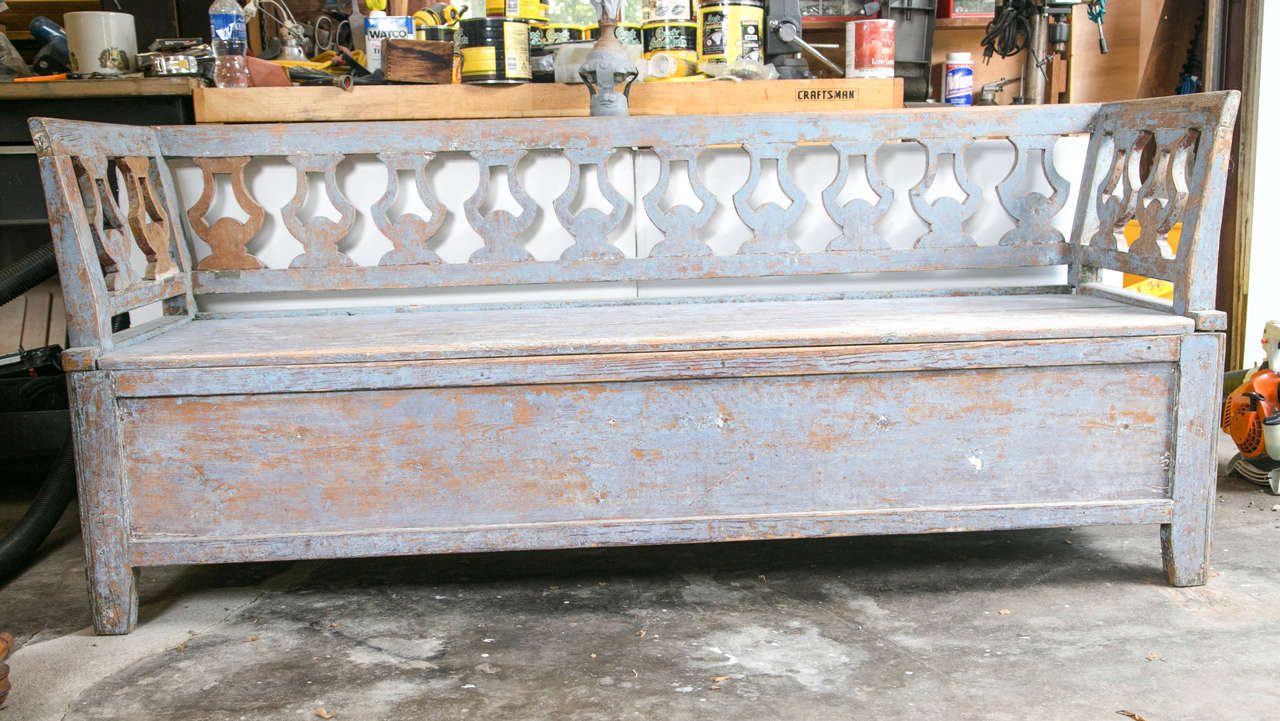 An antique Swedish bench with a carved lyre design back and arms. The seat lifts for ample storage below. The original painted finish is a lovely pale blue.