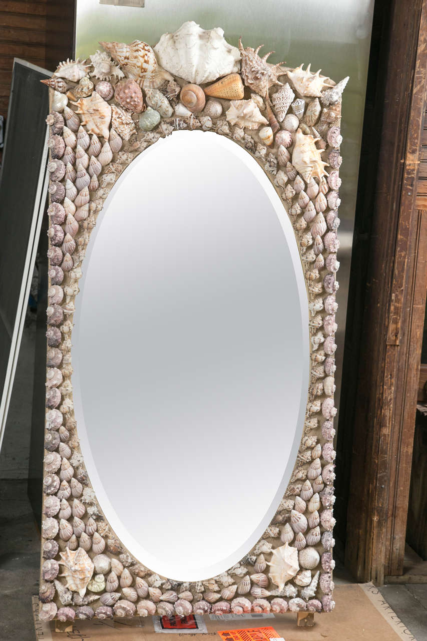 A stunning rectangular wall mirror with a shell encrusted frame and oval beveled glass.