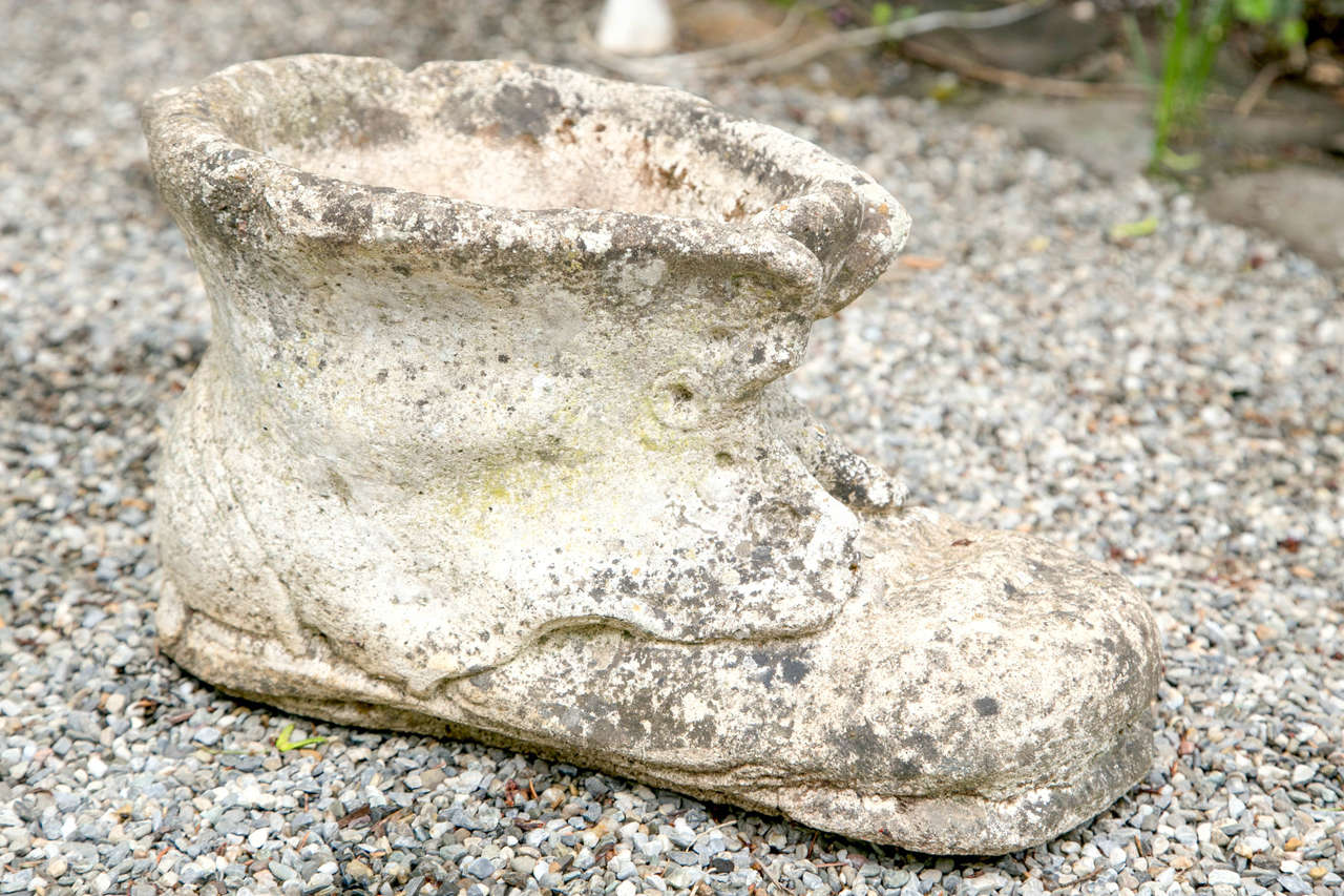An adorable cast stone garden planter in the form of a happily worn in boot. The cast stone has an aged and weathered patina.