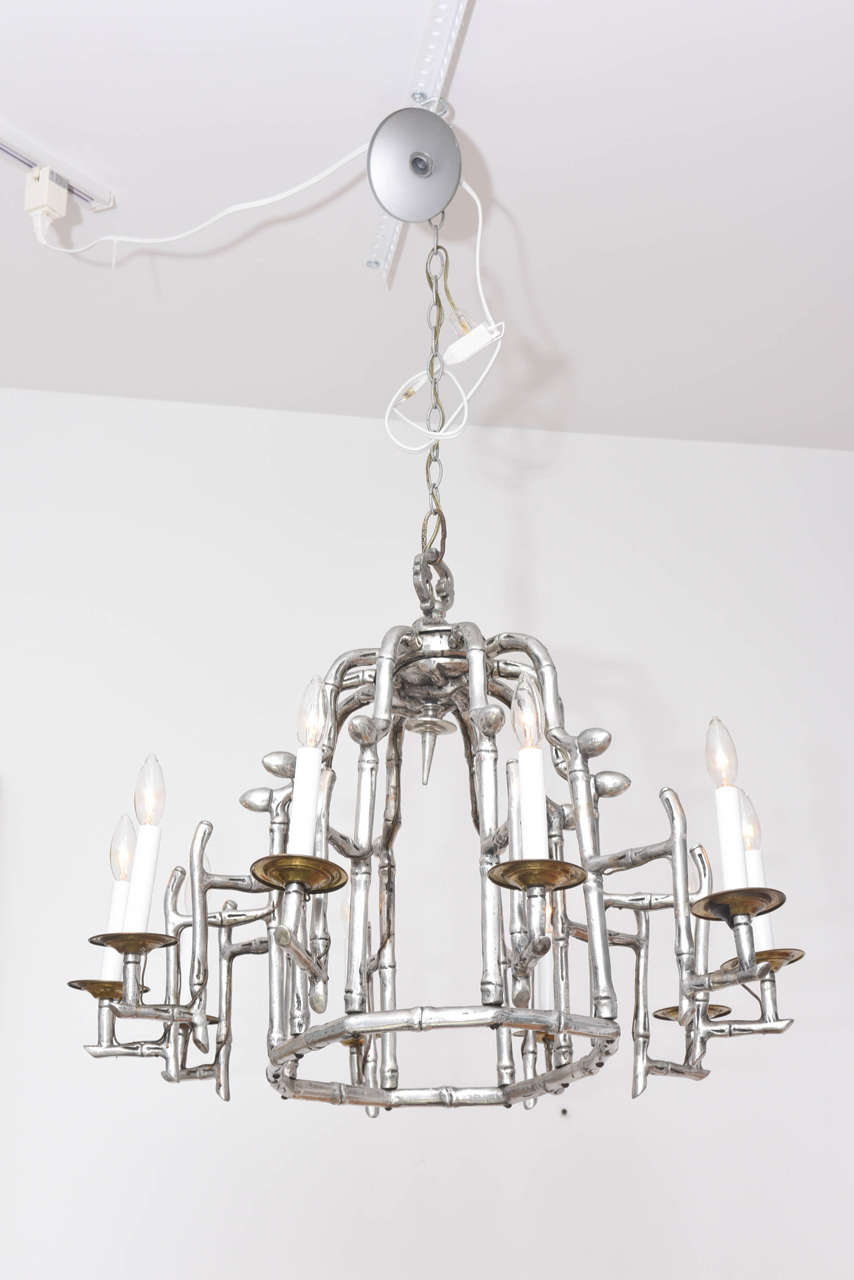 This incredible mid-century faux-bamboo pagoda chandelier from the 1950's is cast in aluminum but takes on the look of antique pewter with a low luster finish which sparkles with the light.  There are 10 candle arms with antique brass bobeche's and