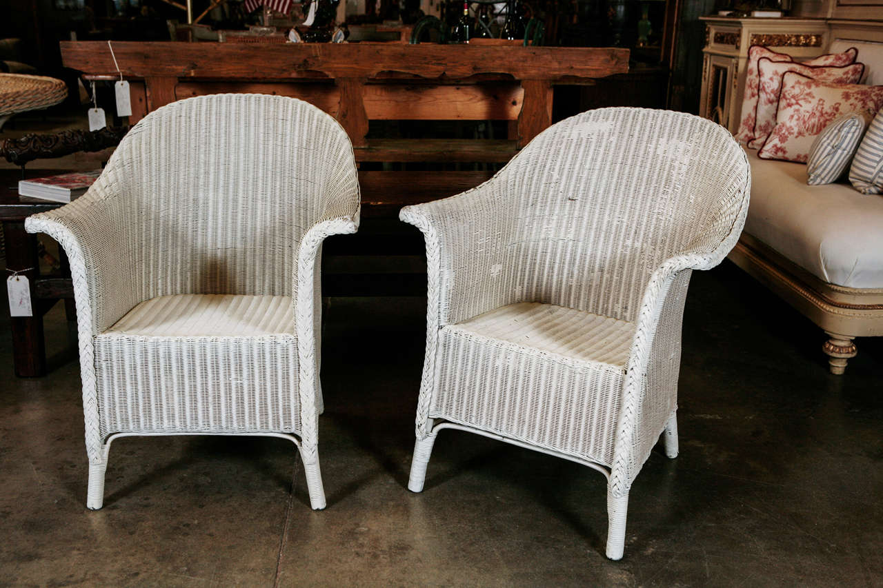 A good pair of American Lloyd Loom arm chairs, circa the 1930's, painted in white with an older blue under coating. The chairs are good quality and very sound in structure. One chair has a label for  