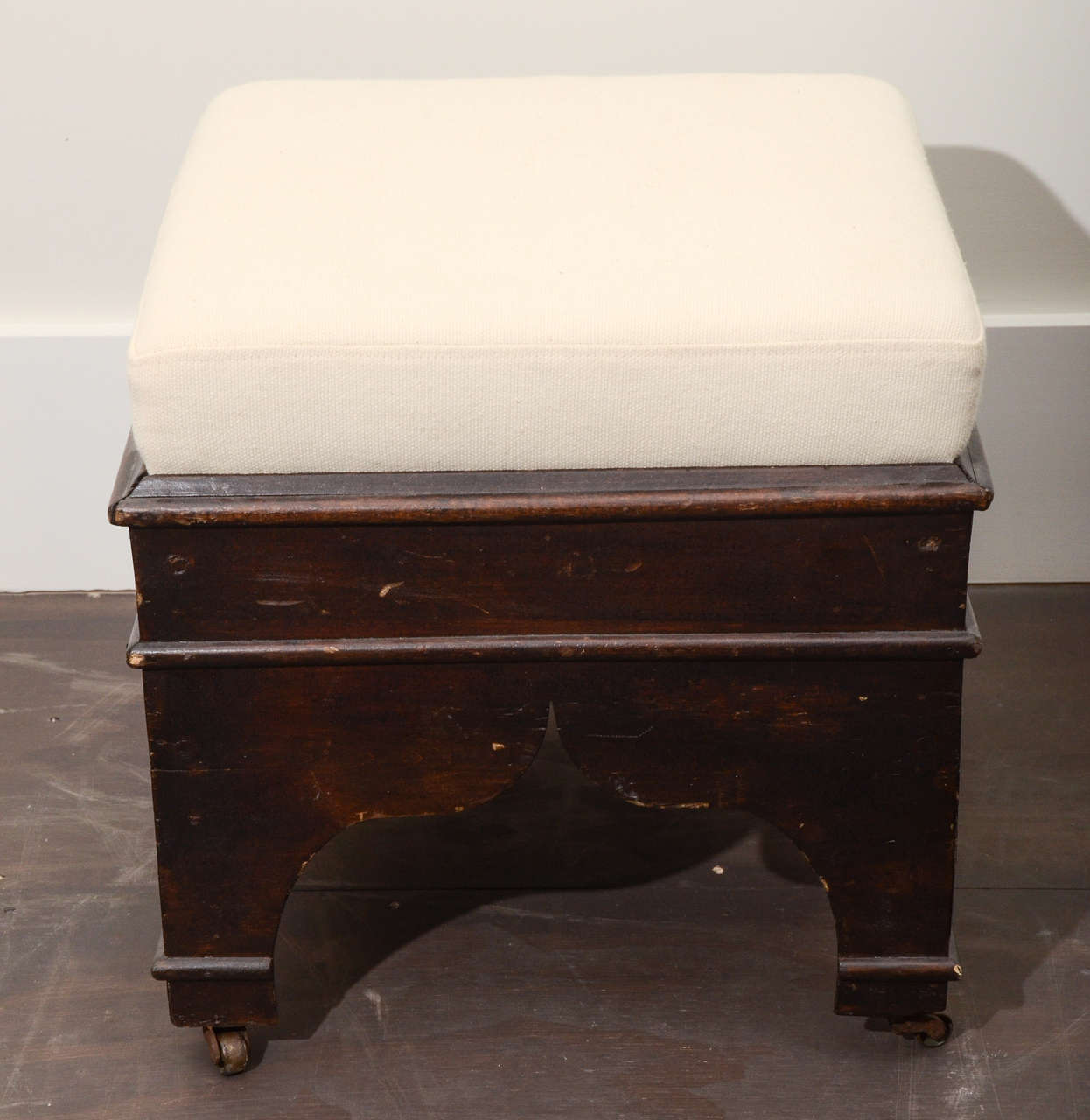 Vintage hand-carved wooden stool with cream upholstery, United States, c. 20th century. 

This petite yet highly charming stool consists of a darkened base with Moorish hand-carved details and cream upholstery. Sits on brass casters.