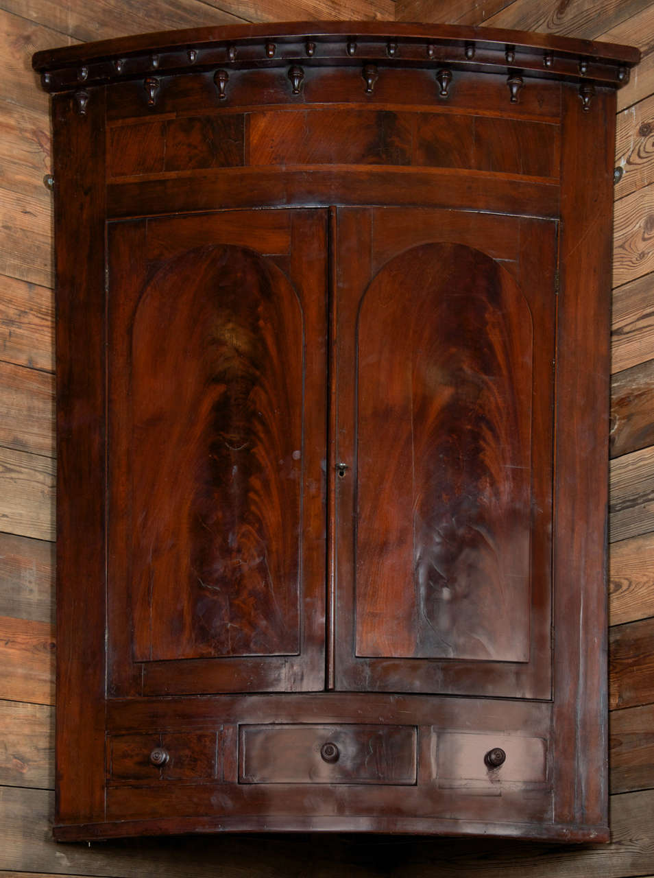 A large and spectacular antique Georgian corner cabinet featuring outstanding in-laid flame mahogany. This late-eighteenth century cabinet has a lovely bowed front with two doors featuring arched panels of stunning matching flame mahogany, which