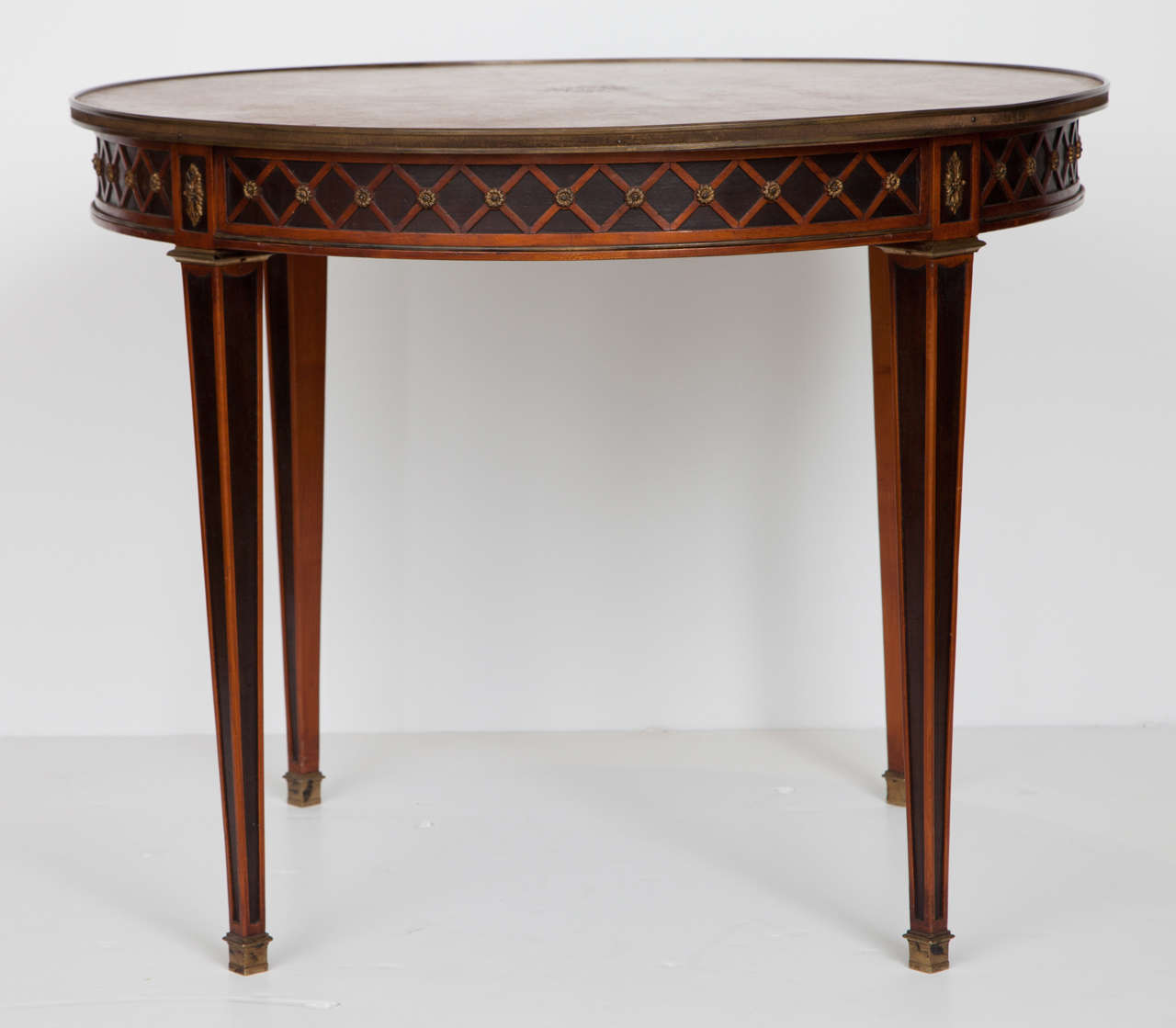 A Louis XVI style gueridon of exceptional quality and workmanship. Attributed to Maison Jansen, this table has ebonized, tapered legs and apron, with a lovely X-pattern overlay, gilt bronze accents and a leather top.