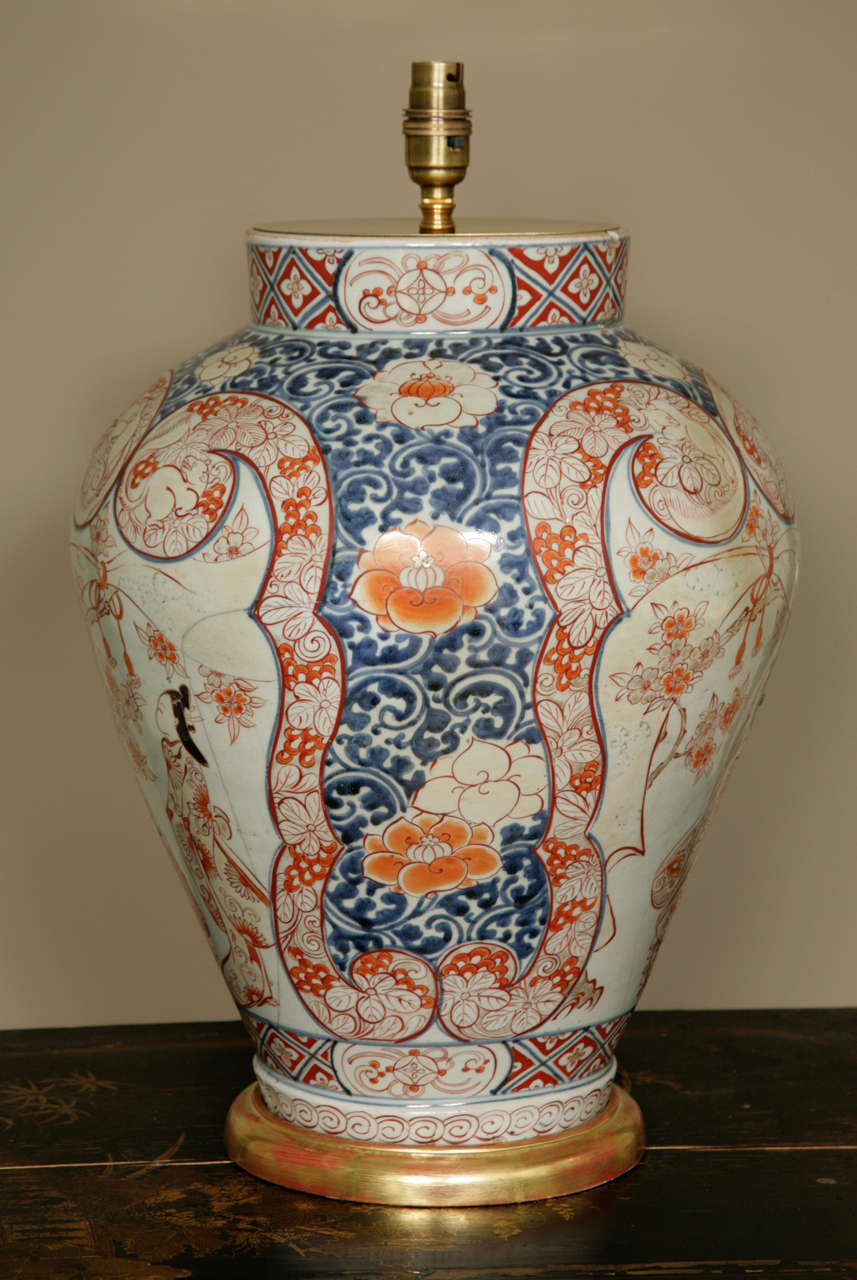 A large 17th century lamped decorated Japanese Imari baluster vase on a hand carved and water gilt wooden base. The vase has been fitted with an antiqued brass plate with a light final. The vase is decorated in separate panels and a floral border.