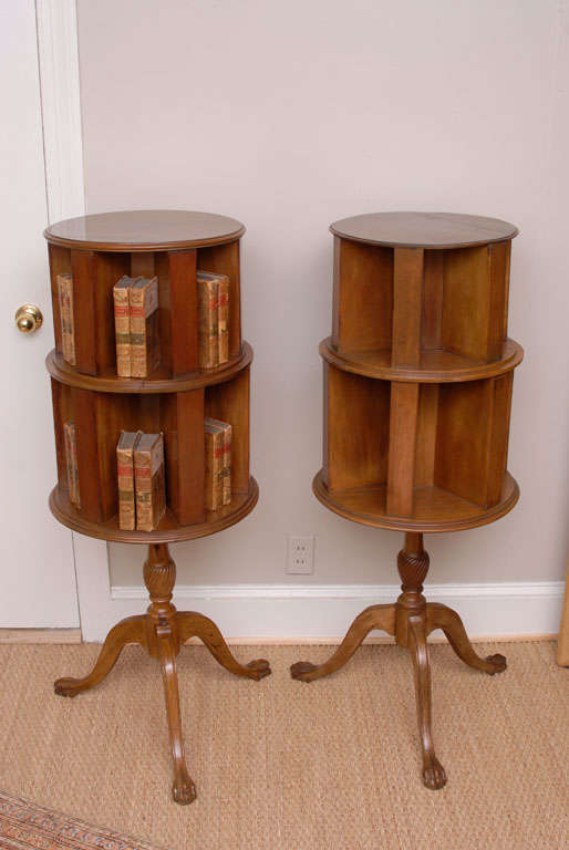 These rare Edwardian period revolving bookcases beautifully exhibit the artistry and ingenuity of English furniture makers. The two-tiered, Neoclassical style cases sit on turned column tripod bases ending with carved claw feet.