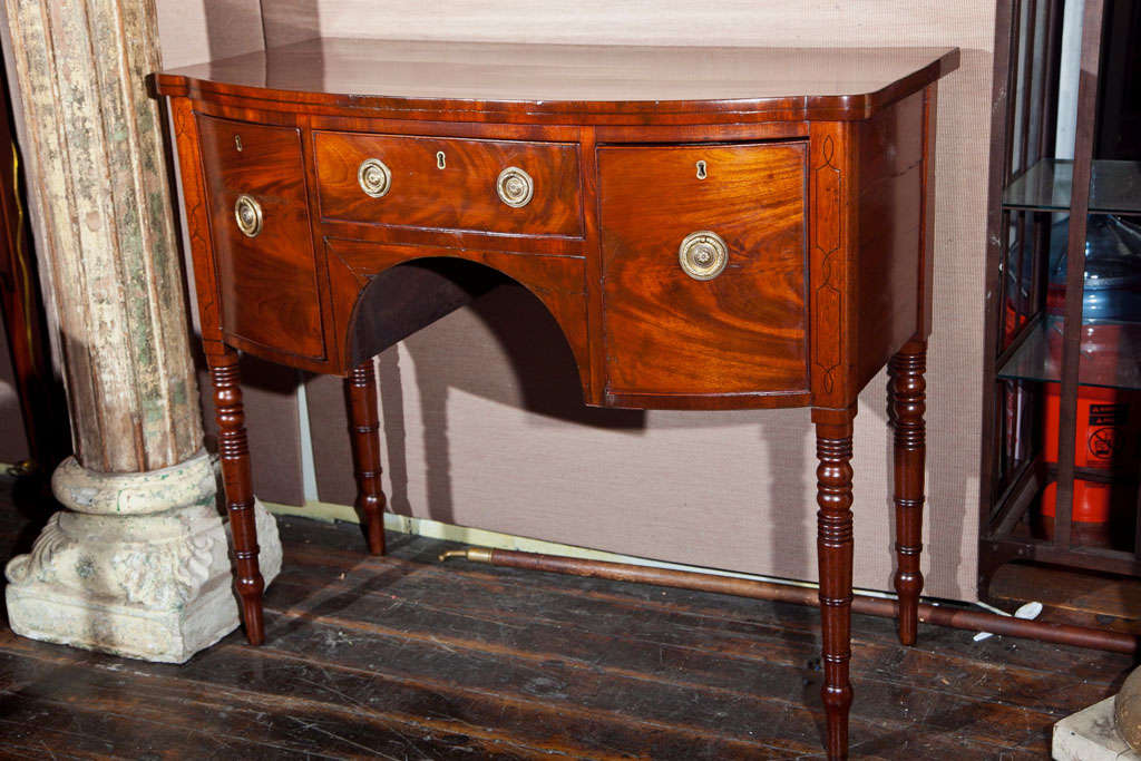 A Bowfront, mahogany sideboard with turned legs and bottle drawer.