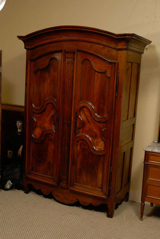 A petite French Country armoire in hand carved and richly patinated walnut features Louis XVI details. Flame walnut inserts decorate the door panels. The doors and apron have French Provincial scalloping. The spacious interior has one shelf and