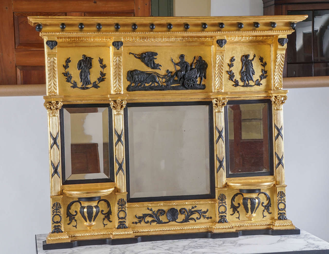 A truly exceptional circa 1800 George III English Regency neoclassical style bichrome giltwood and gesso overmantel mirror having top cavetto-and-ebonized-ball cornice surmounting three panels with acanthus corbels headed by ebonized ram's heads;