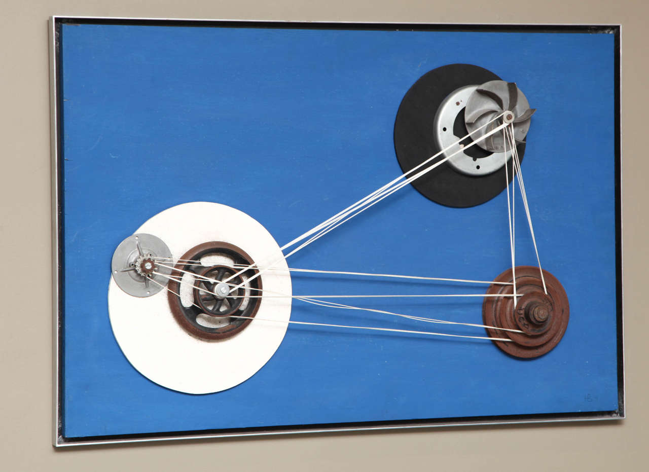 A blue-painted wood surface with wood and steel wheels, gears and pulleys applied and connected with nylon cording. By Hedi Baum (Germany/US 1908-1989) signed with initials and date 1971 LR, signed ink on reverse. In aritist-supplied welded aluminum