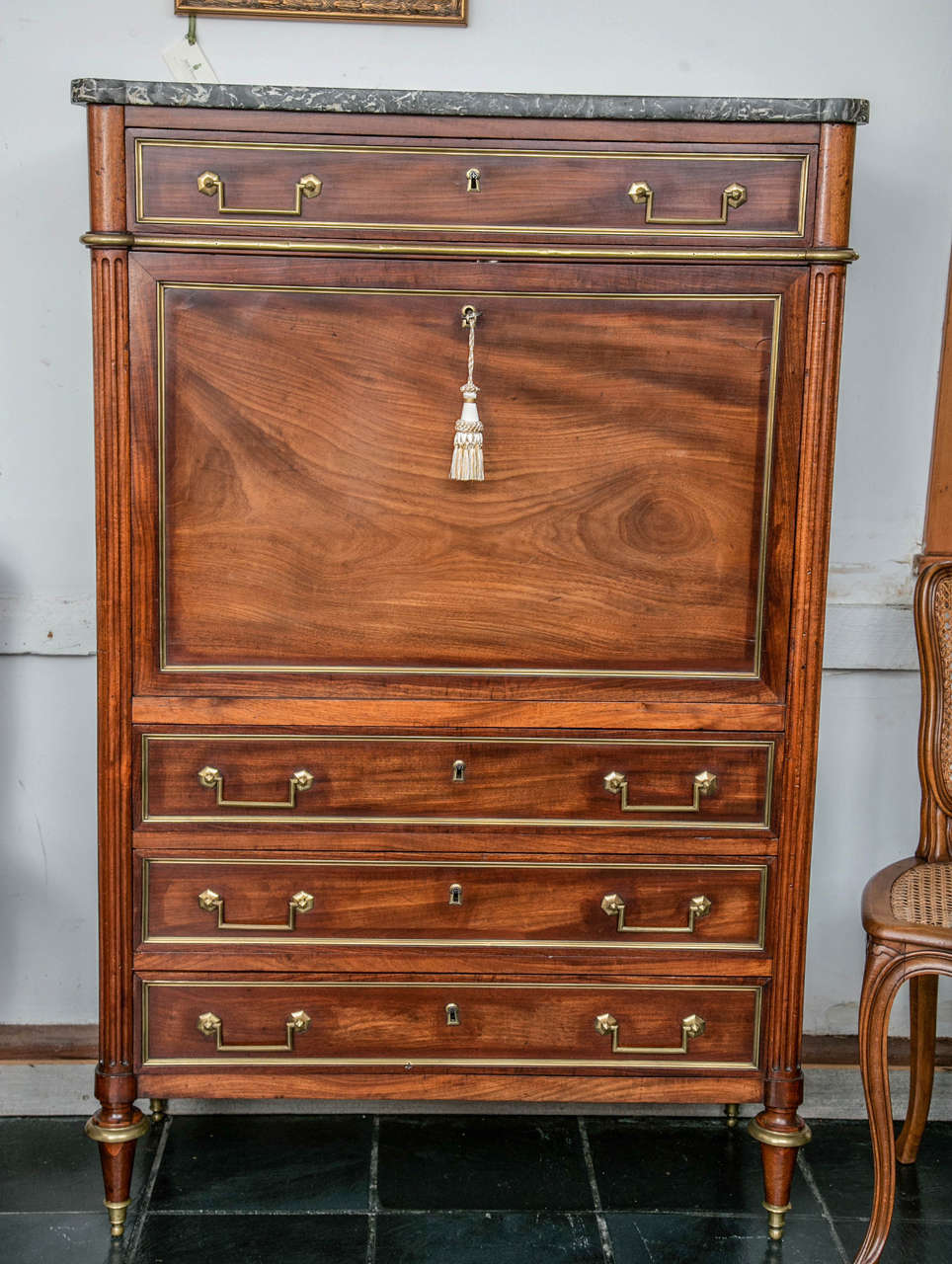 This mahogany abattant has wonderful proportions and it has aged to a warm fruitwood tone. Looking every bit the French desk, it wears a mantel of marble and brass trim to the case, while fluted columns flank the case and lead down to turned feet.