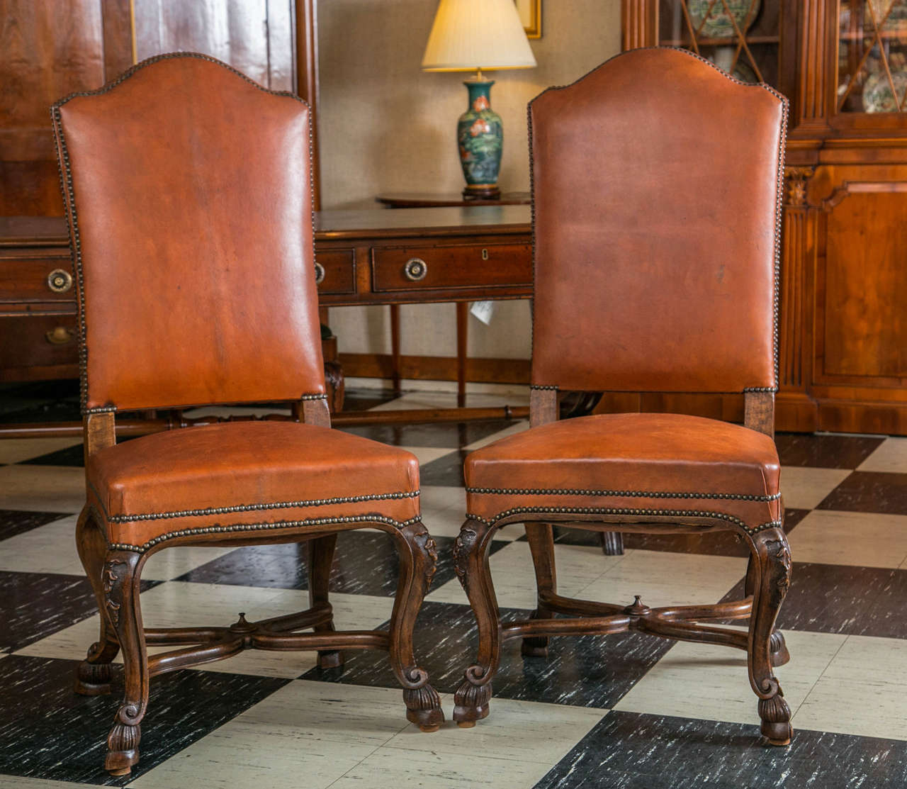 Cinghiale leather with nailhead trim give these chairs great character, however, the carving of the frames is what is remarkable about these copies of 18th century chairs. The richly carved knees draw the eye down to the shaped, crossed stretchers