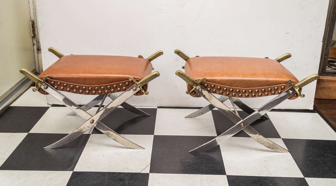 Pair of Mid-20th century campaign style sword benches. Leatherette upholstered seats and trimmed in nail heads. Decorative brass handled swords as X-form legs.