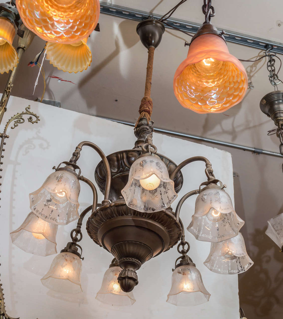 For those who complain about not enough light in an area, here we have a hard to find eight-arm chandelier. The warmly patinated bronze body is accompanied by a matched set of period stencil etched glass shades. The rope covering the pole is