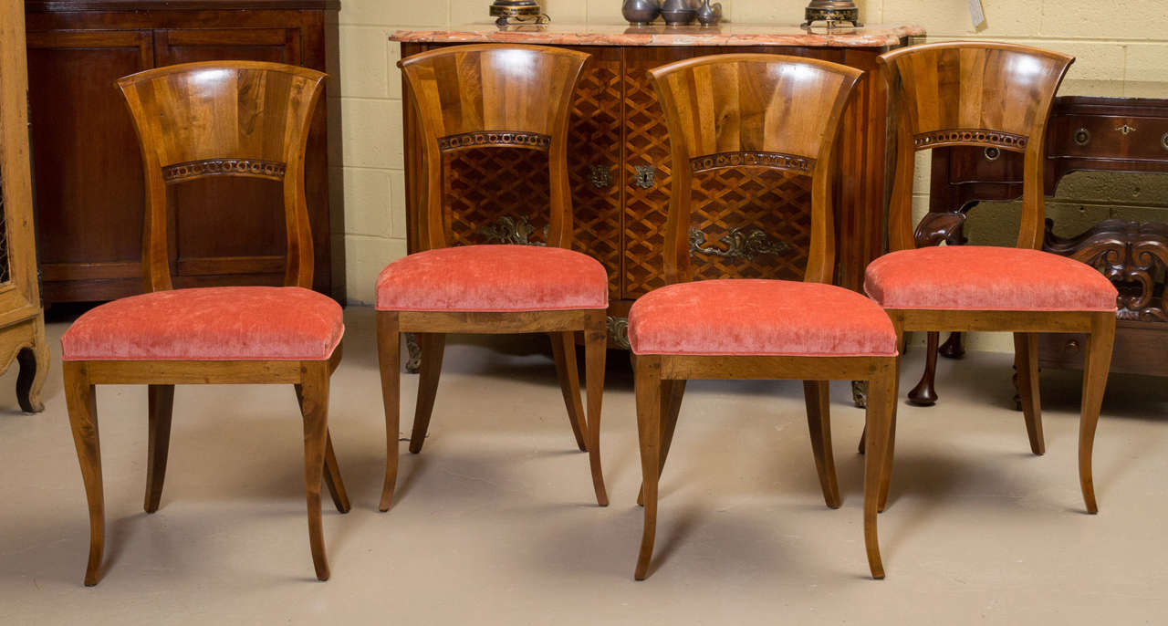 A beautiful set of four walnut Biedermeier style side chairs. These chairs have a curved flat top crest rail with circular carving below. Upholstered in red velvet above the seat rail that leads to tapered saber front legs and square canted rear