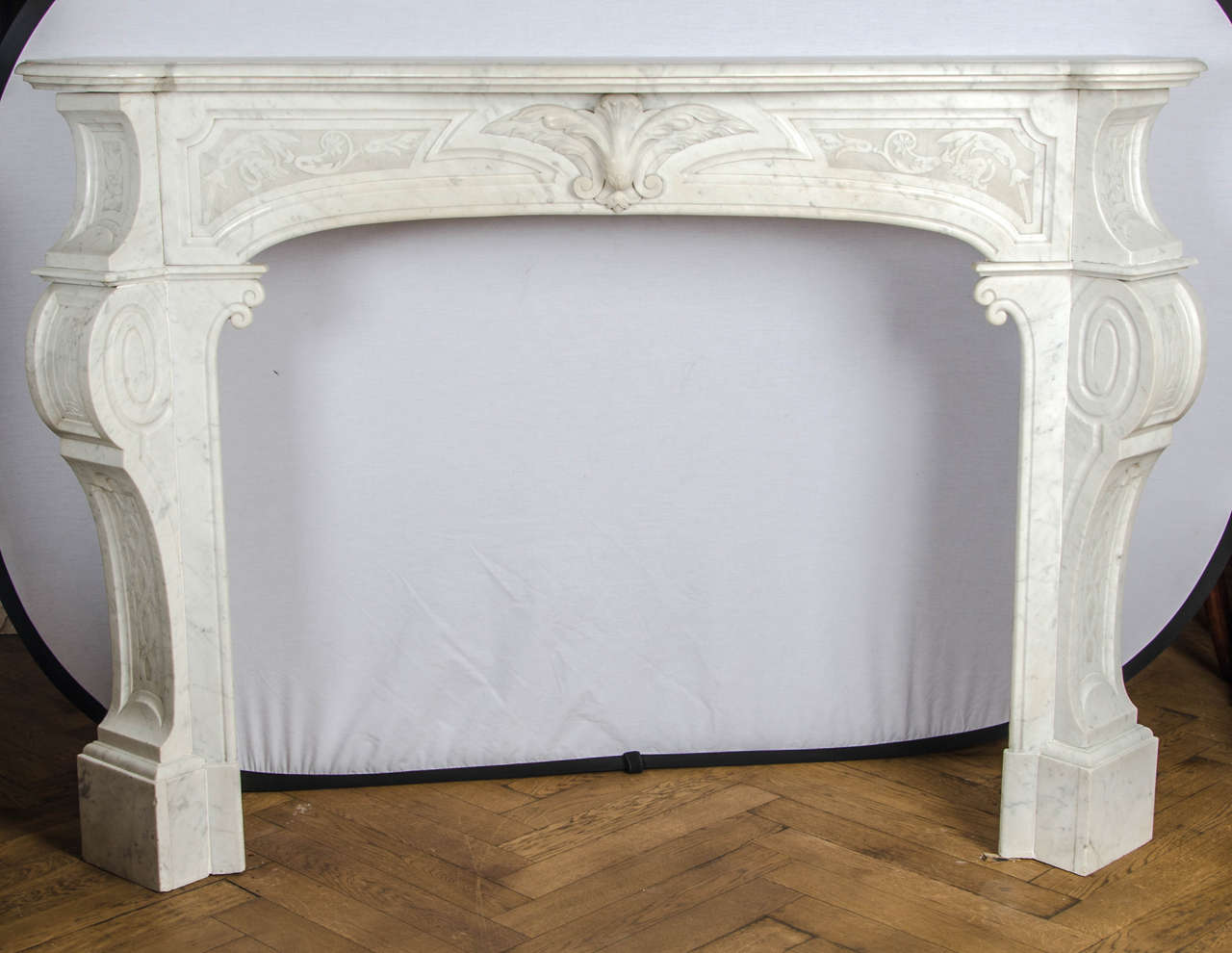An antique marble fire surround in the style of Louis XV. This Carrara marble surround features s erpentine shelf atop angled, cabriole scrolling jambs which are decorated with finely carved designs of foliate and floral motifs. 

The opening