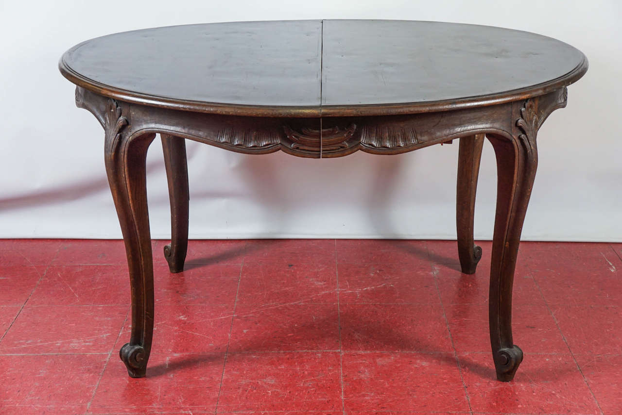 Late 19th century oval dining table has a scalloped apron with hand-carved drapery and urns on four sides and cabriole legs with spines ending at the top with splayed leaves. The top has a banded border. The table is made to extend with an iron