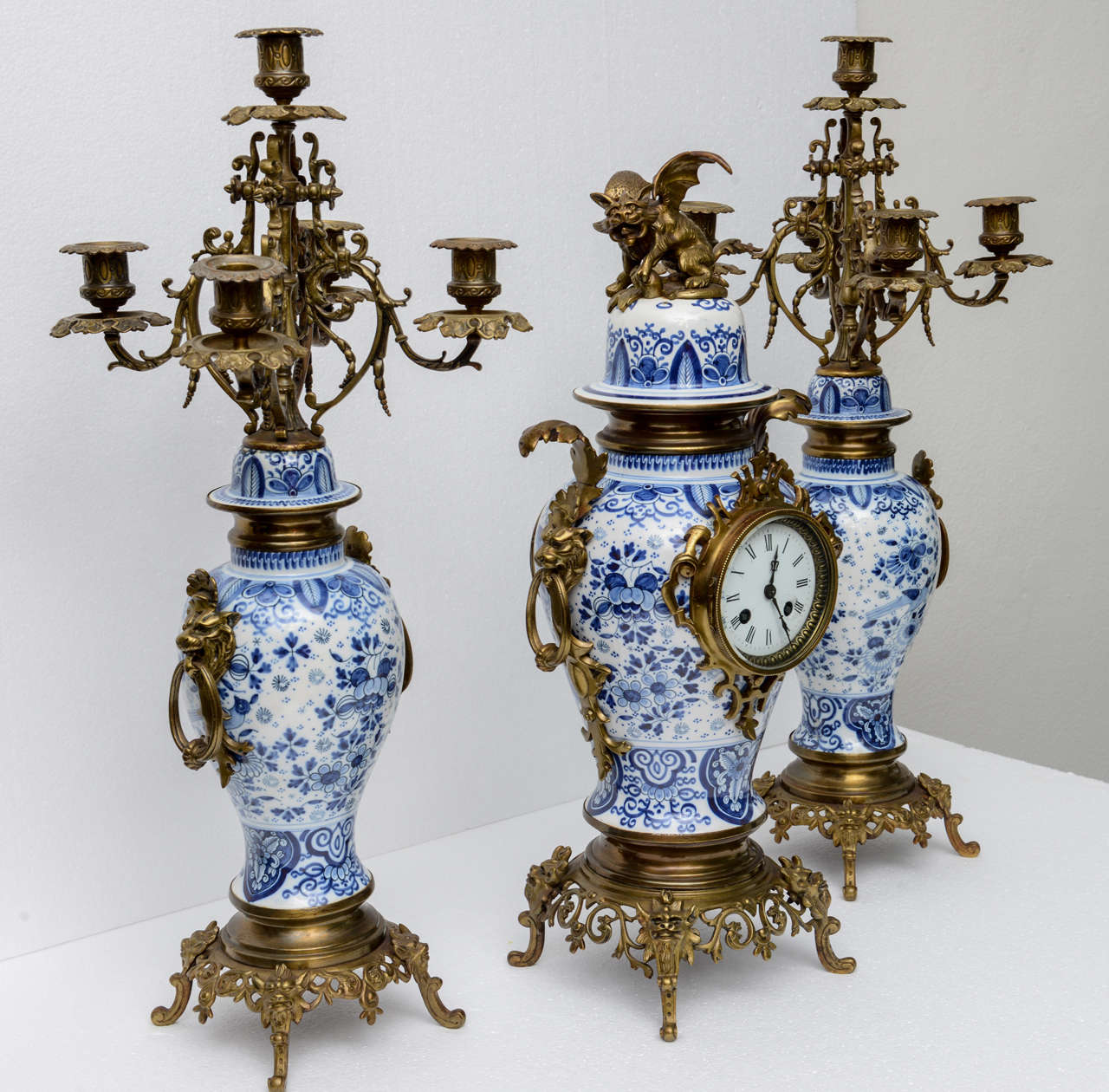 Delft garniture with bronze mounts; garniture consists of three pieces, a clock ( 21.5h) and a pair of candelabras (24.5h) enameled dial signed, 