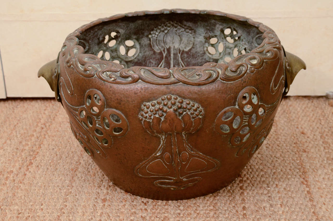 This rare German Art Nouveau, or Jugendstil, planter has a hand-hammered copper body executed in the Japanisme taste with low relief stylized lotus flowers, undulating wave forms with pierced circles throughout, a raised wave form rim, and flanking