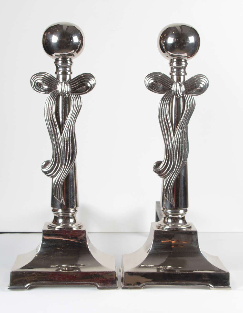 Fantastic pair of Art Deco andirons in polished nickel with cannon ball finial and stylized bow.