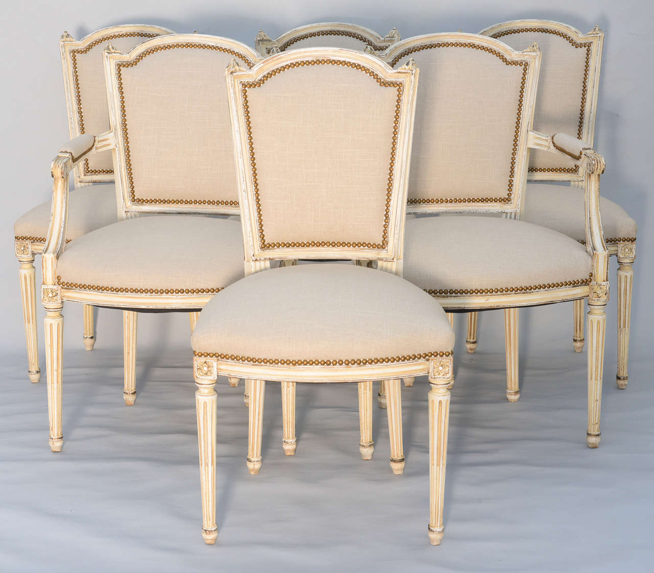 Set of 6 dining room chairs (two armchairs and four side chairs), distressed painted finish, each having domed padded backrest and crown seat upholstered in linen with nailheads; raised on round fluted legs. (Side chairs are 20