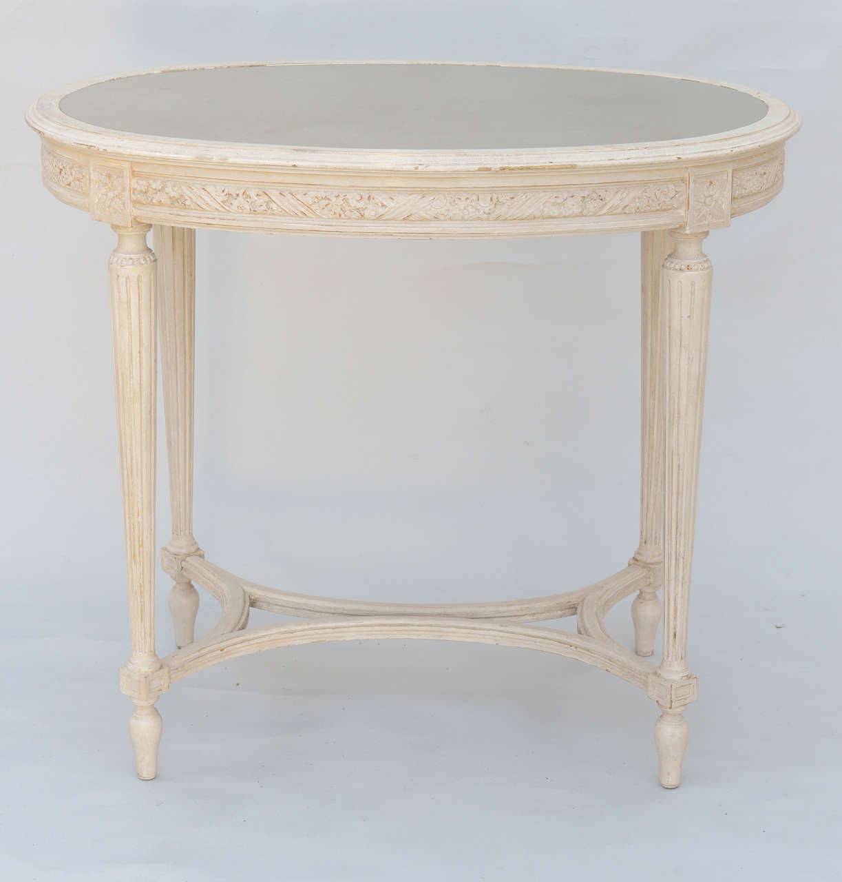 Oval accent table, Louis XVI form, having distressed painted finish, spotted mirror top inset in frame, intricately carved apron, round fluted tapering legs connected by curved stretcher.