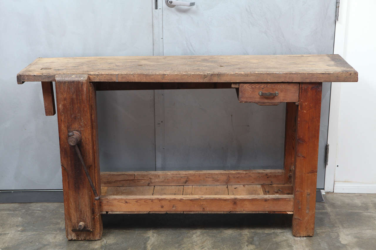 This is an interesting English Carpenter's work bench having seen years and years of service. This bench has one small drawer and a vertical wooden vice with metal fittings. The work bench stands on square legs having stretchers with a bottom tool