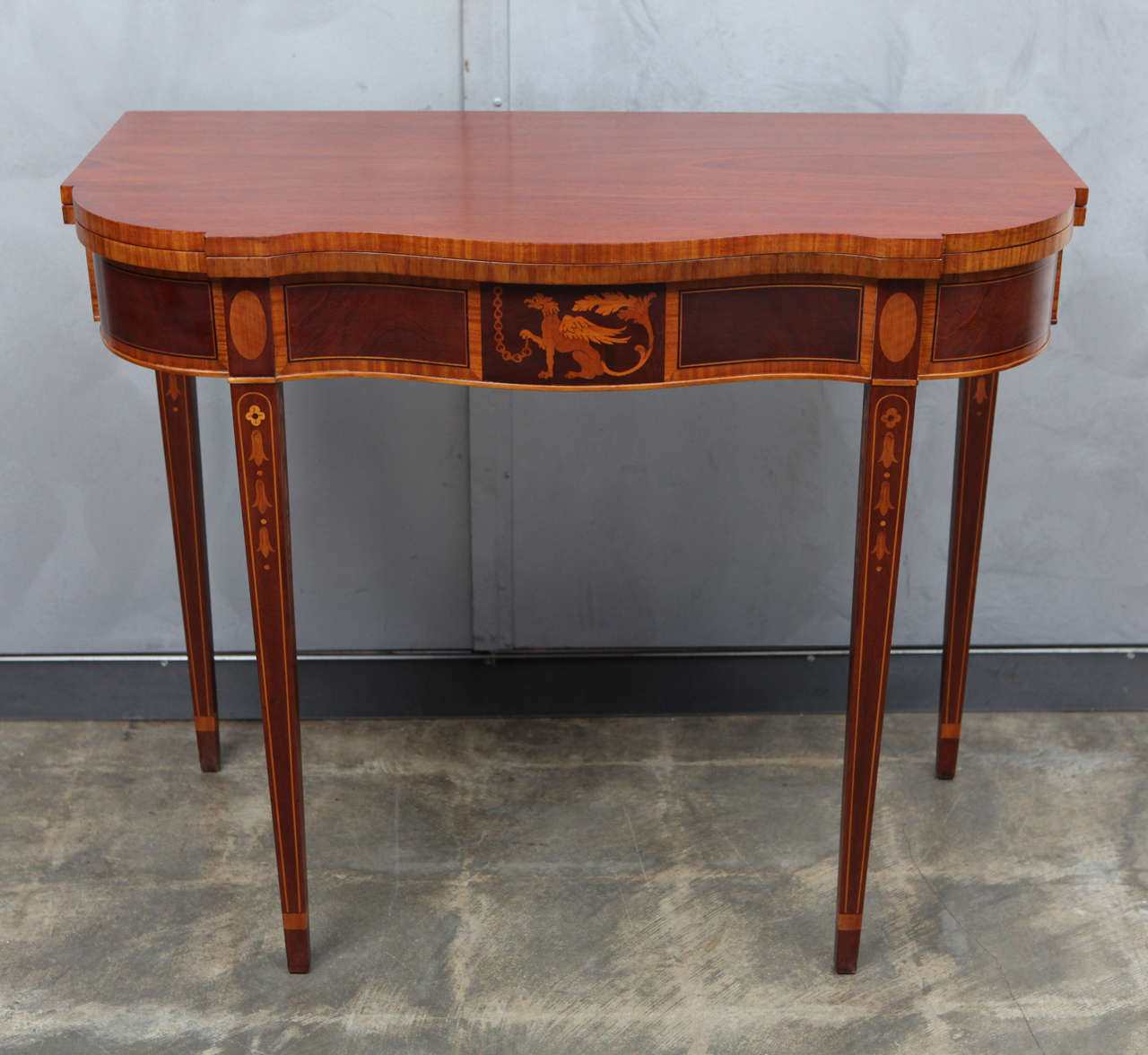 This inlaid mahogany game table has some great examples of federal style motifs and techniques including a griffinin inlaid marquetry and parquetry banding and details. The four tapered legs are beautifully decorated with bell flower details. This