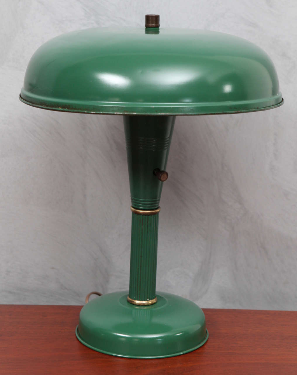 This is a wonderful Deco/Modern green painted desk lamp that reflects the design movements of the mid 1930's. The lamp's ridged center column with polished brass rings highlight the combination of modern or industrial elements with art deco charm.