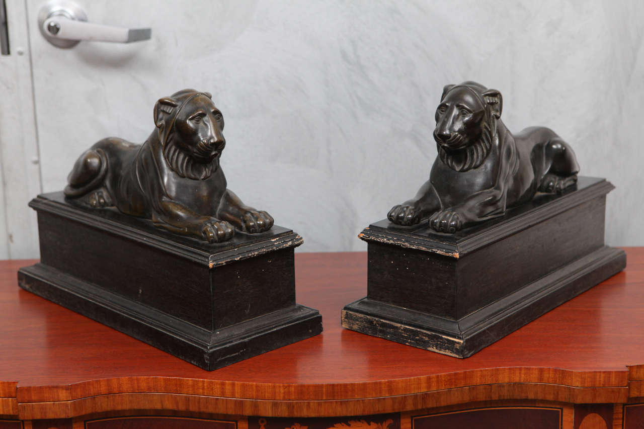 These wonderfully crafted bronze recumbent lions on wooden pedestals are a rare example of the design influence of Egyptian art and sculpture in Europe during and resulting from the period of the Grand Tour. During this time the aesthetics from the