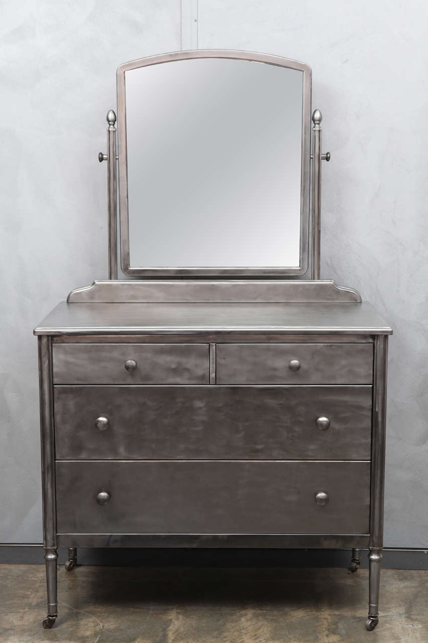 Art Deco/Modern Style 1930's brushed steel dresser with original arched top pivoting mirror. This chest of drawers has two over two drawers with painted interiors and original knob pulls. The swiveled mirror is framed with a nice beveled border and
