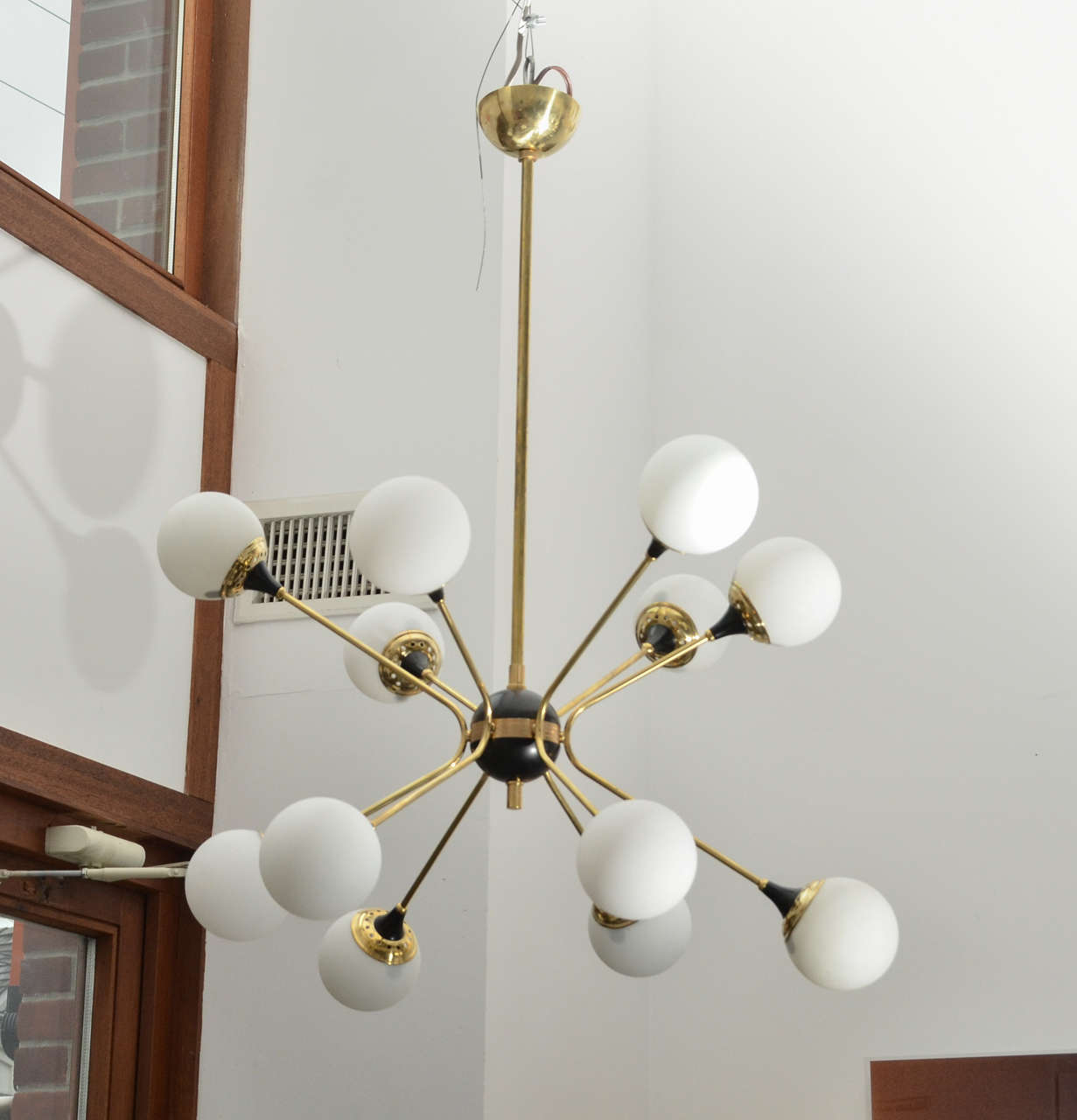 A black round sphere holding six bent brass arms ending with twelve handblown glass shades.