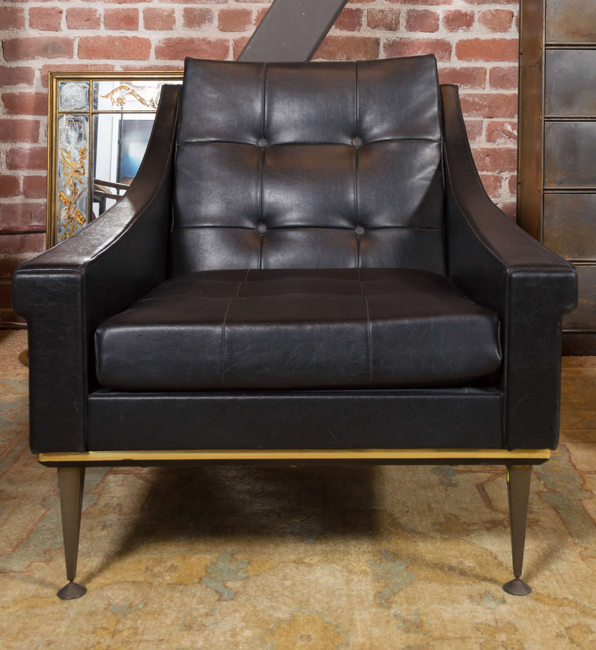 Pair of black leather club chairs having tufted backs and gold details.