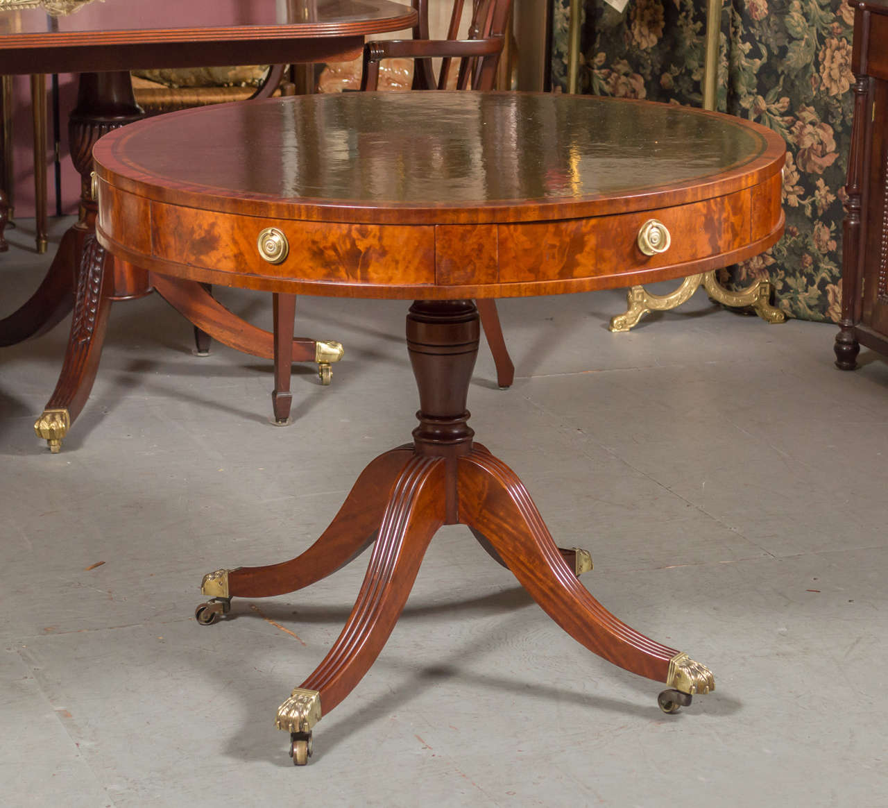 English drum table (also called a rent table), with swivel mechanize of the wooden collar type. With tooled Black leather surface, and two drawers and two dummy drawer (alternating), graceful reeded down swept legs ending in Brass claw feet on