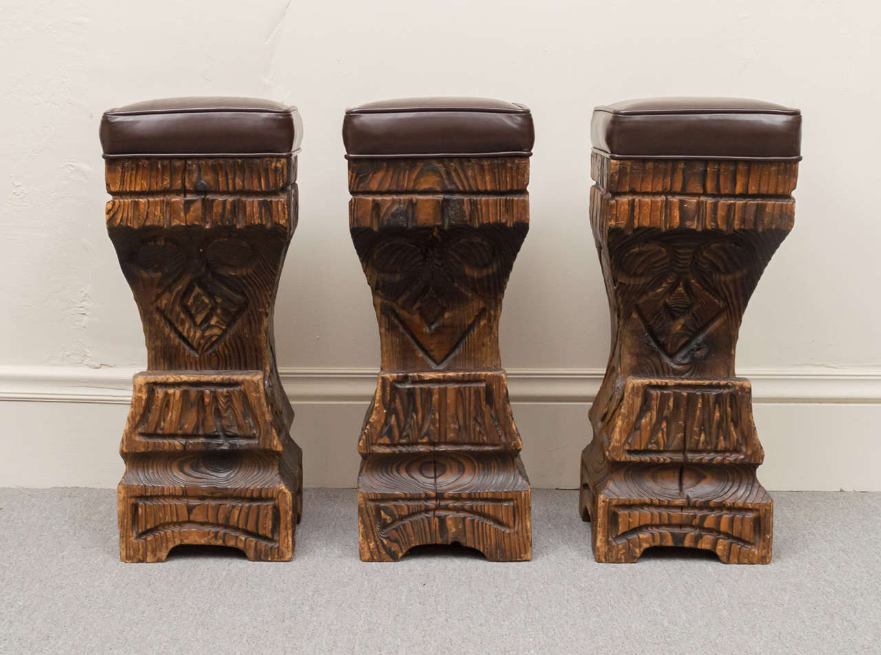 Set of three substantial, solid wood construction bar stools. Each stool is one piece of solid wood that has been carved in a South Pacific primitive style. New dark Brown leather seats top them off. Great set for a Tiki or Man Cave space.