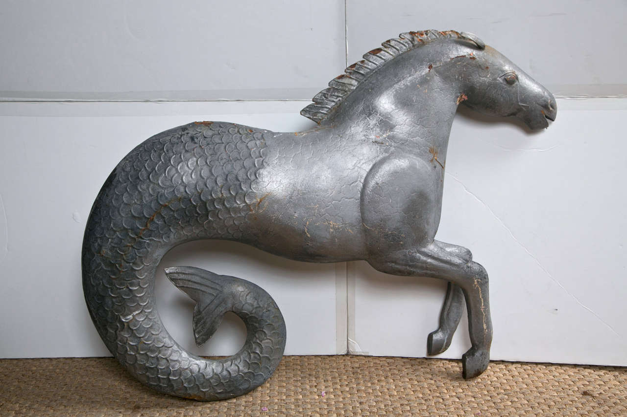 The hippocampus, the steed of the sea god Poseidon, combines the  body of  horse and the tail of a sea creature.  This silvery painted folk art creation  has some rust.  It may have been used as a tavern as there are 2  small holes on the upper edge