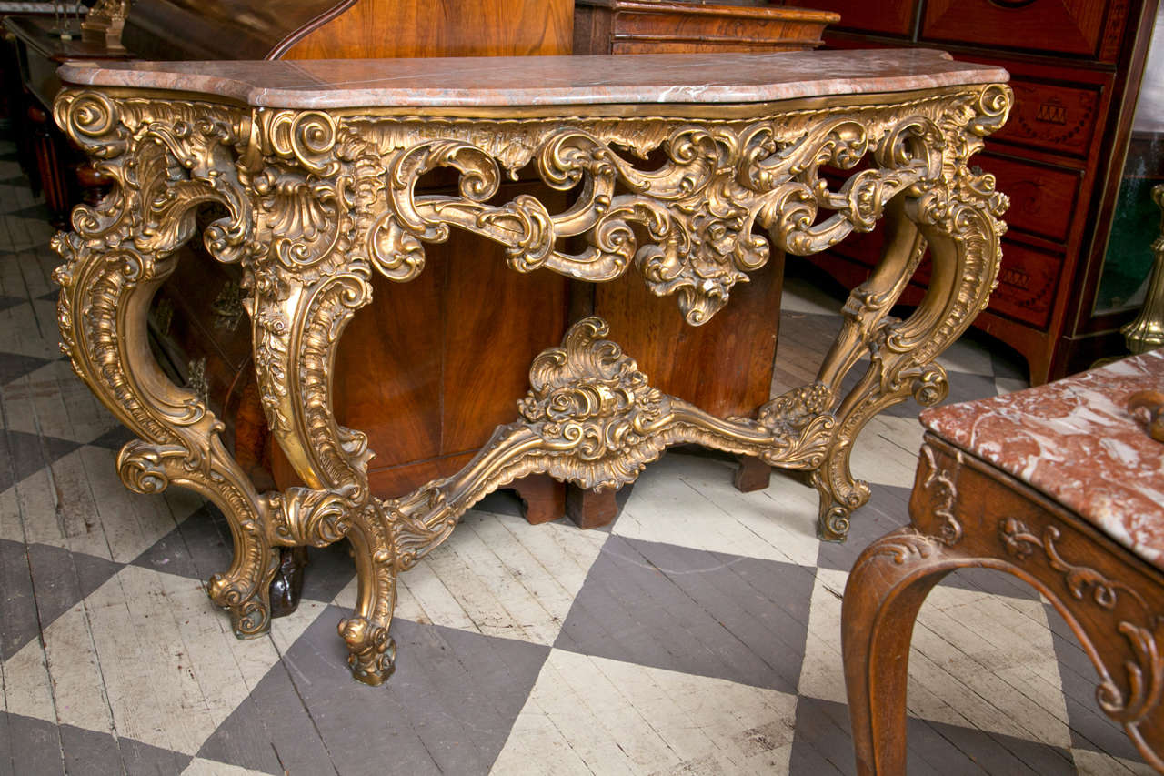 A deeply carved  wood and  gilt  console  table with conforming marble top.
Four  cabriole legs joined by a central stretcher surmounted  by a deeply carved  wave form finial.  Large C scroll and S scroll carvings,  pirecings and   shell forms.The