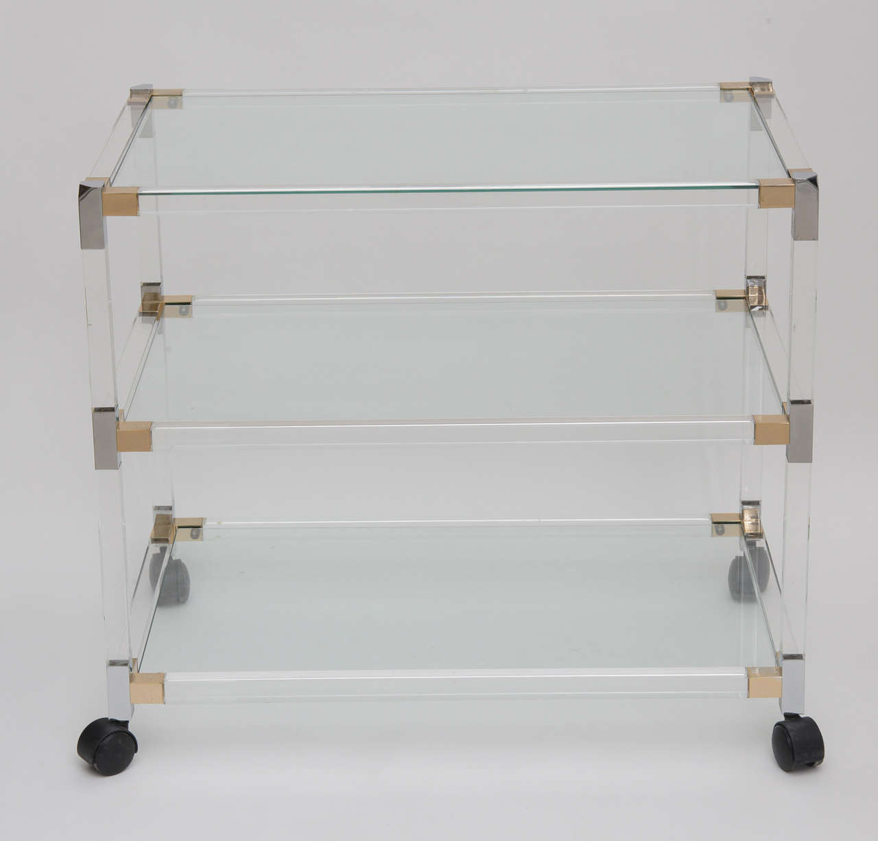 Vintage lucite bar cart with two- tone chrome and brass geometric corner accents. The trolley has three glass shelves for barware.